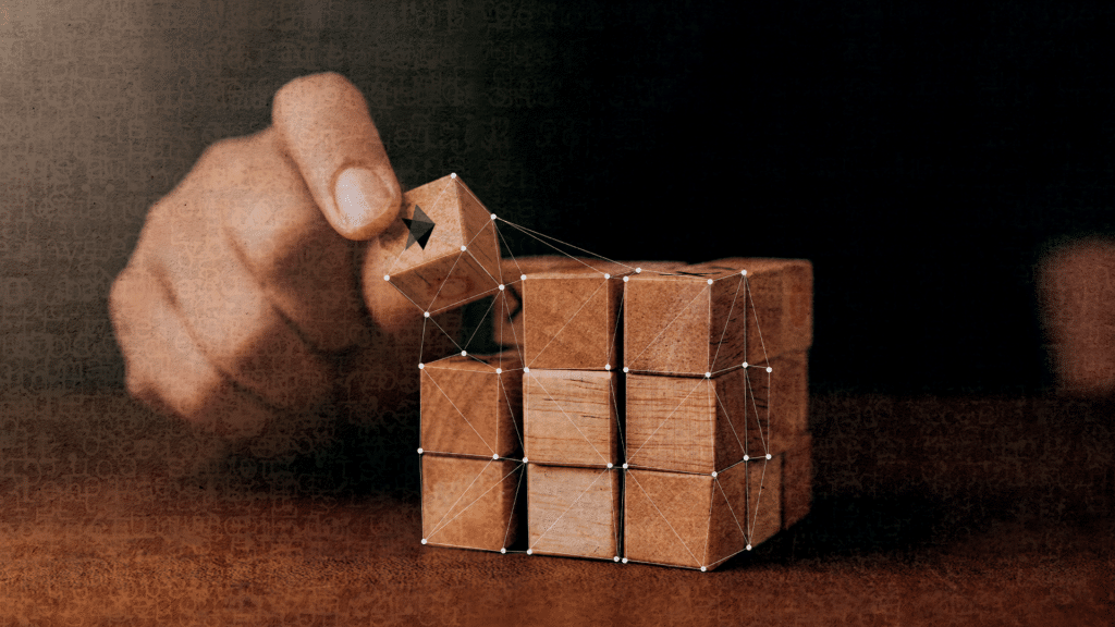 The image shows a hand placing a wooden cube on a stack of other cubes. There is a network of lines and dots overlaying the cubes, suggesting connections between them.